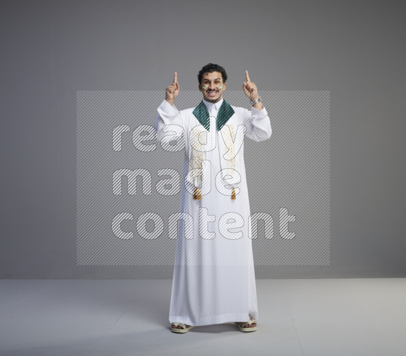 رجل سعودي يرتدي ثوب ابيض يضع شال مكتوب عليه المملكة العربية السعودية حول رقبته