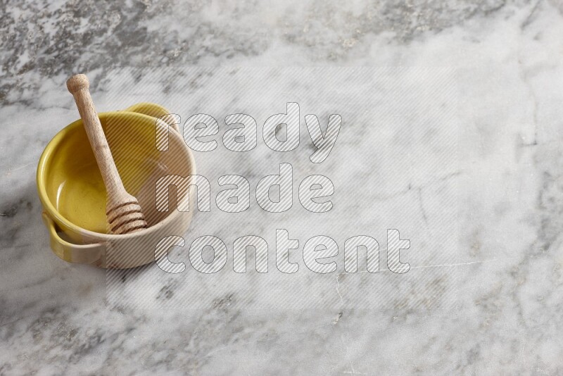 Multicolored pottery bowl with wooden honey dipper in it on grey marble background