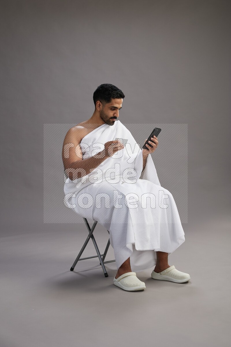 A man wearing Ehram sitting on chair holding ATM card on gray background