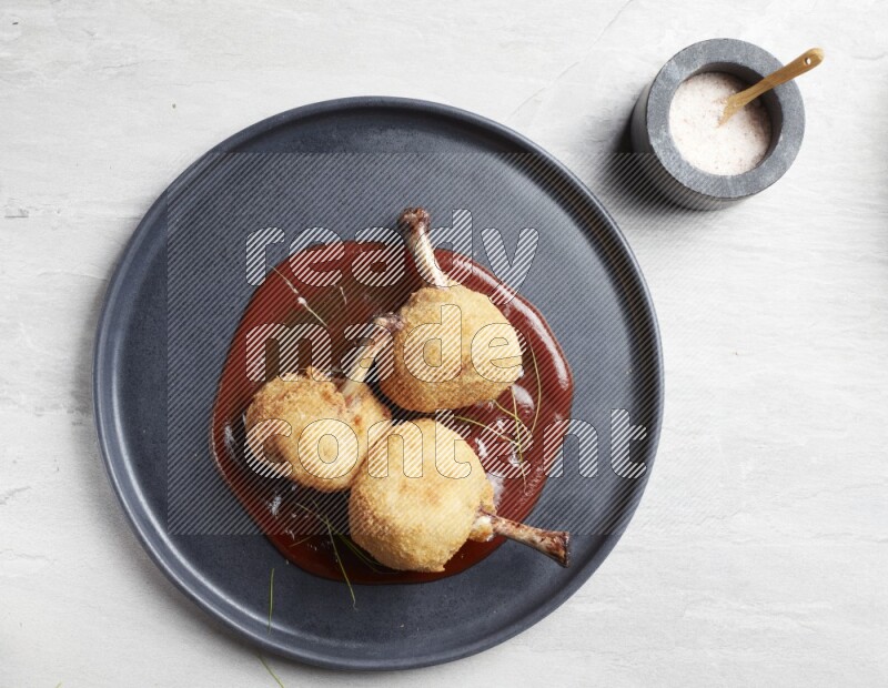 breaded drumstick on round dark grey pottery plate on grey textured countertop