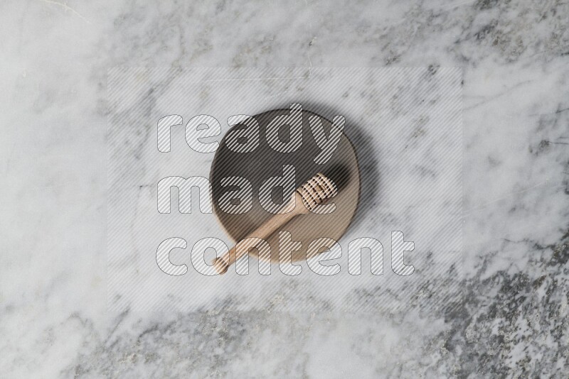 Multicolored pottery plate with wooden honey dipper in it on grey marble background