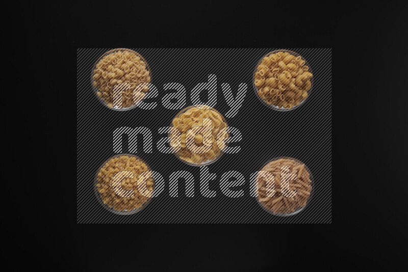 Different pasta types in 5 glass bowls on black background