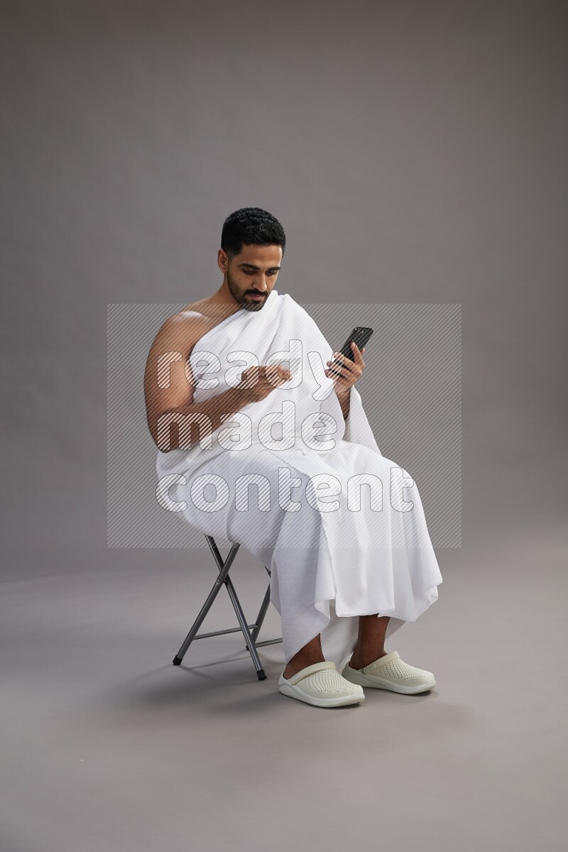A man wearing Ehram sitting on chair holding ATM card on gray background