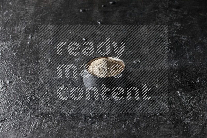 Black pottery bowl full of white pepper powder on textured black flooring
