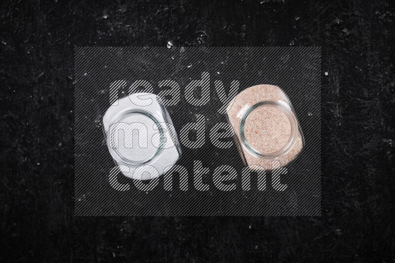 2 glass jars one is filled with fine himalayan salt and the other with table salt on black background