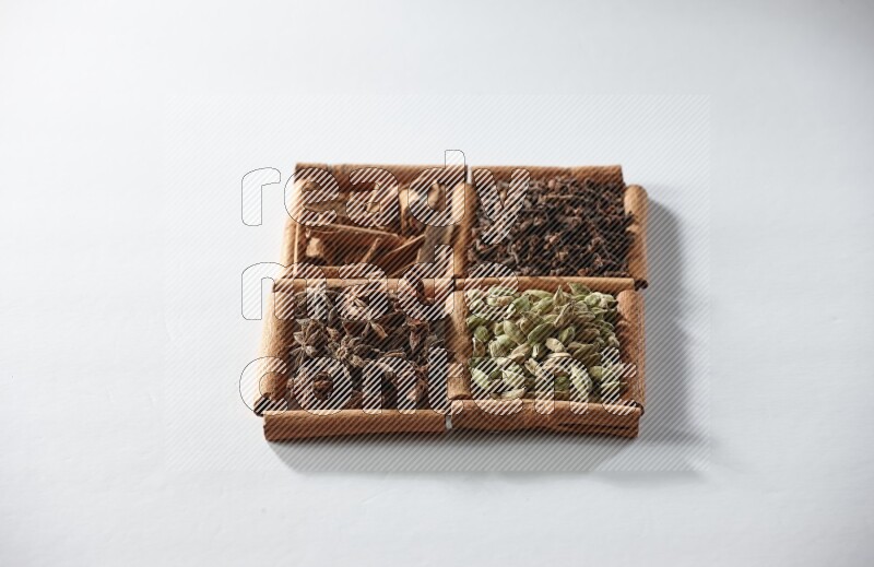 4 مربعات من أعواد القرفة ممتلئة بالهيل واليانسون النجمي والقرنفل والقرفة على أرضية بيضاء