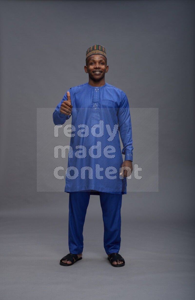 Man wearing Nigerian outfit standing interacting with the camera on gray background