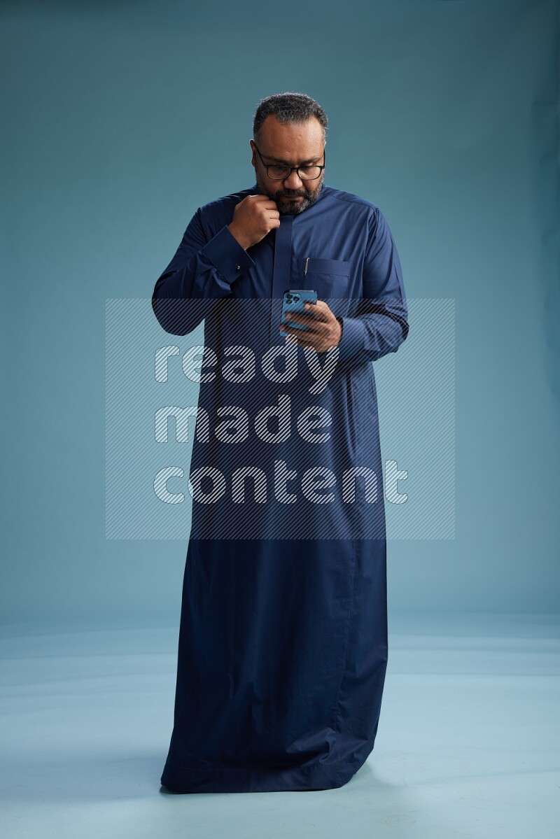 Saudi Man without shimag Standing texting on phone on blue background