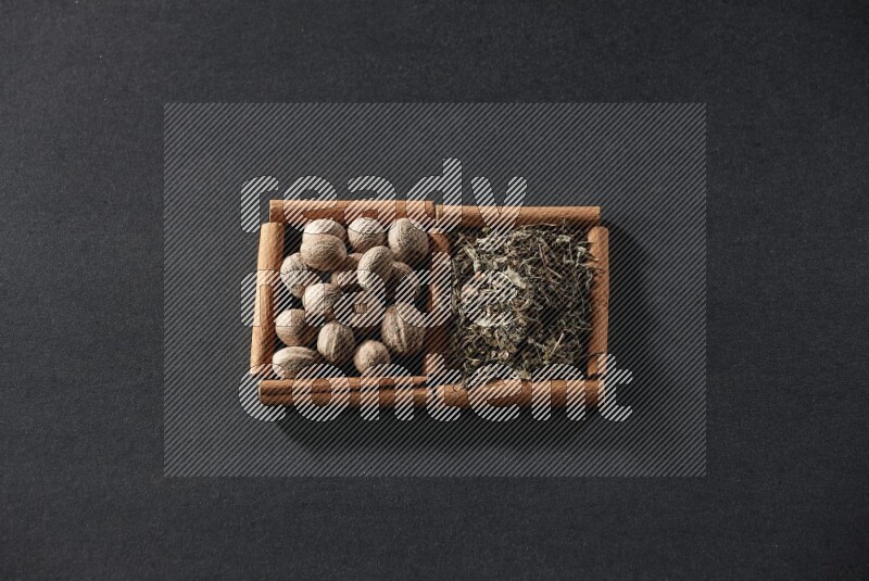 2 squares of cinnamon sticks full of nutmegs and dried basil on black flooring