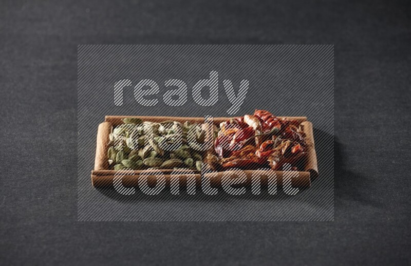 مربعان من أعواد القرفة ممتلئان بالفلفل الحار المجفف وحبوب الهيل علي خلفية سوداء