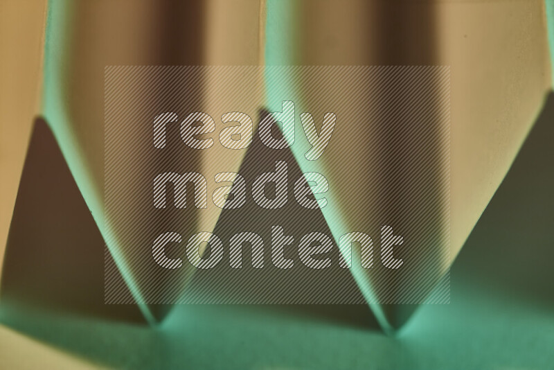 A close-up abstract image showing sharp geometric paper folds in green gradients and warm tones