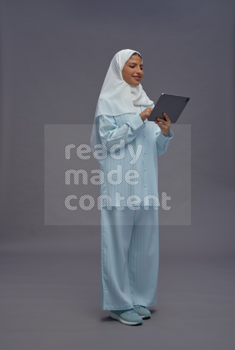 Saudi woman wearing hijab clothes standing working on tablet on gray background