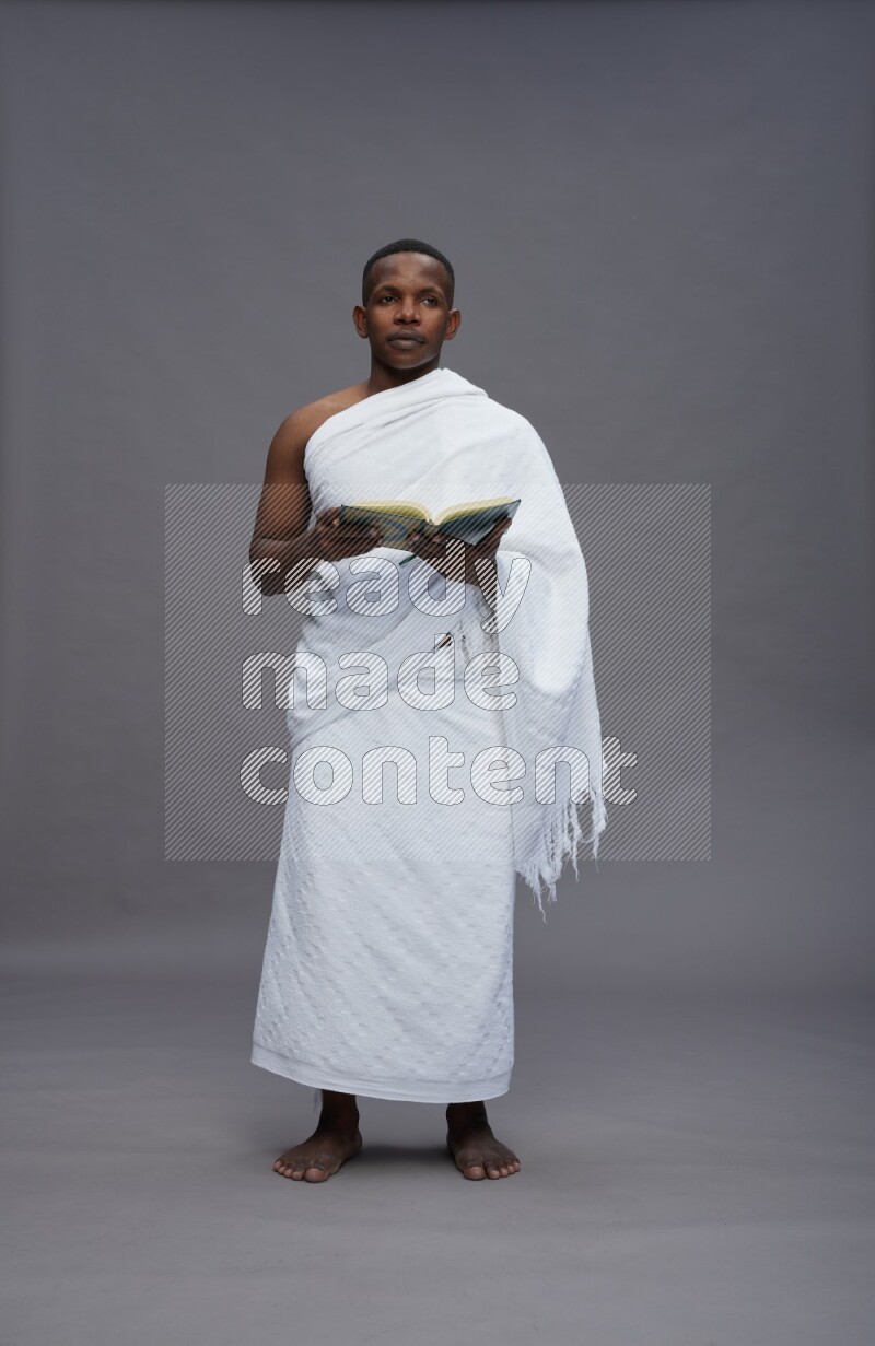 A man wearing Ehram Standing reading quran on gray background
