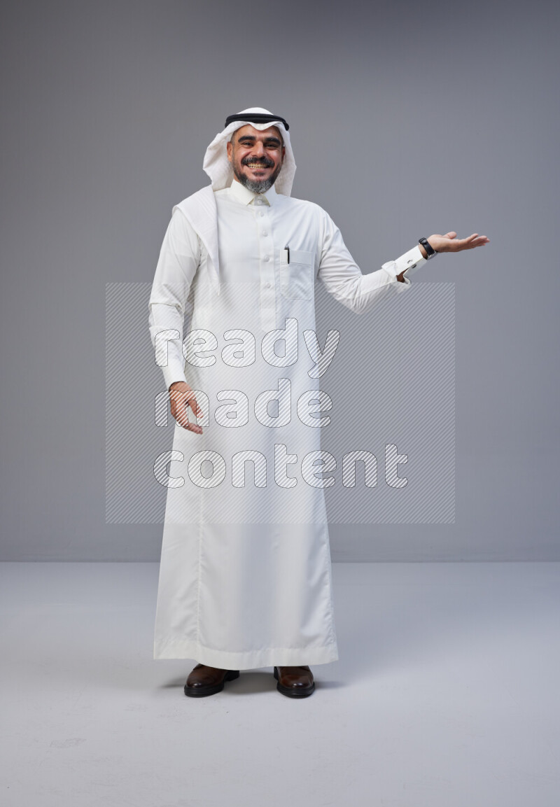 Saudi man Wearing Thob and white Shomag standing interacting with the camera on Gray background