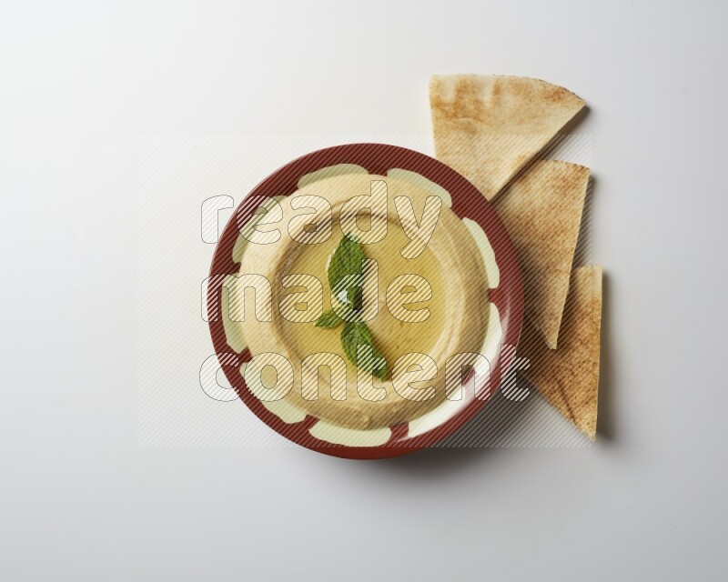 Hummus in a traditional plate garnished with mint on a white background