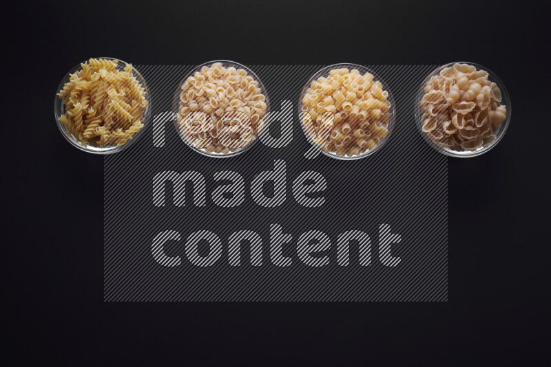 Different pasta types in glass bowls on black background