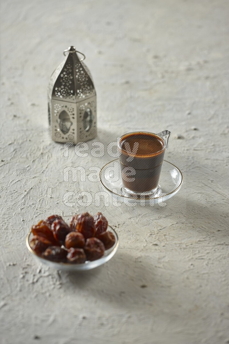 A silver lantern with different drinks, dates, nuts, prayer beads and quran on textured white background