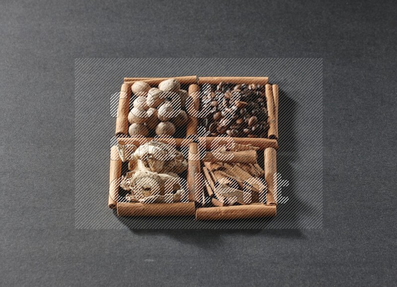4 squares of cinnamon sticks full of coffee beans, cinnamon, dried ginger and nutmegs on black flooring