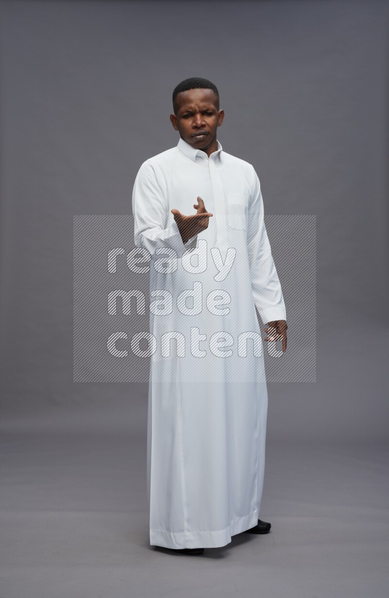 Saudi man wearing thob standing interacting with the camera on gray background