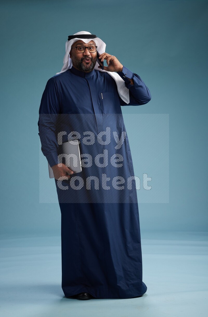 Saudi Man with shimag Standing talking on phone on blue background