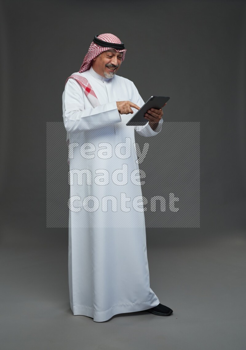 Saudi man with shomag Standing working on tablet on gray background