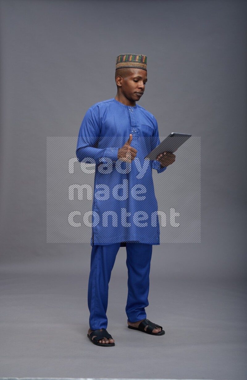 Man wearing Nigerian outfit standing working on tablet on gray background