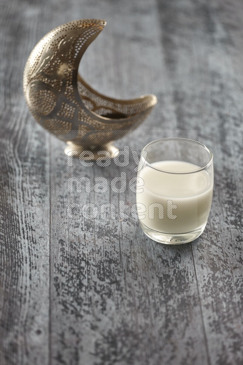 A silver lantern with different drinks, dates, nuts, prayer beads and quran on grey wooden background