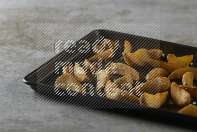 wedges potato in a black stainless steel rectangle tray on grey textured counter top
