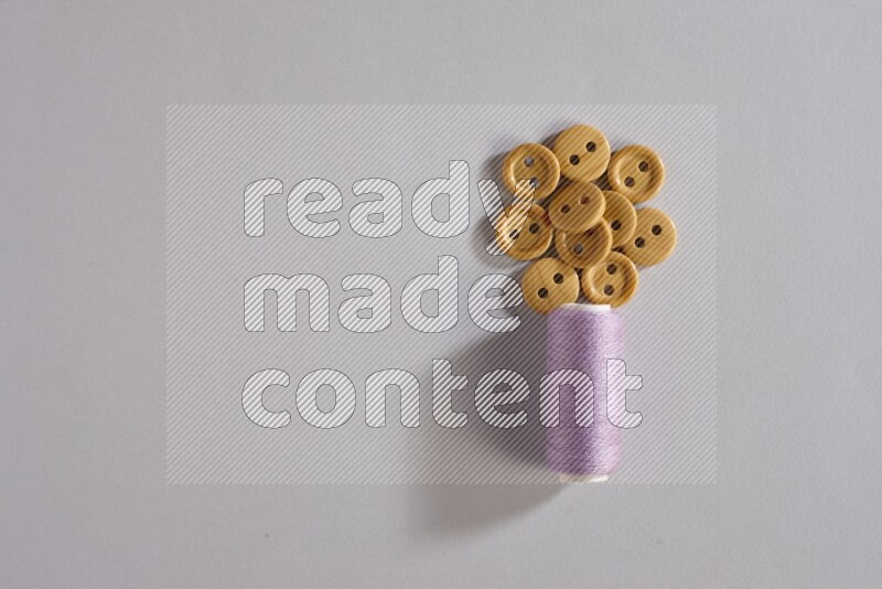 A purple sewing thread spool with small bunch of buttons on grey background
