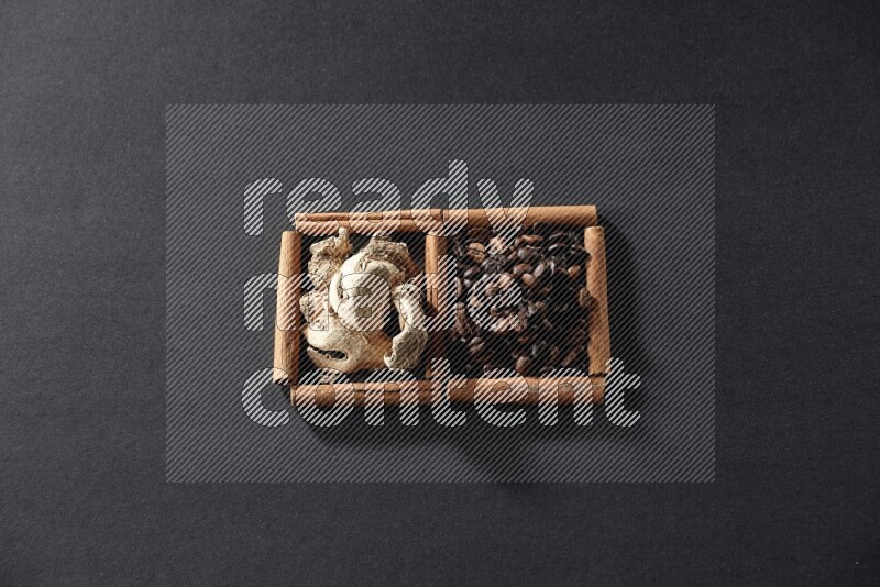 مربعان من أعواد القرفة ممتلئان بحبوب القهوة والزنجبيل المجفف علي خلفية سوداء