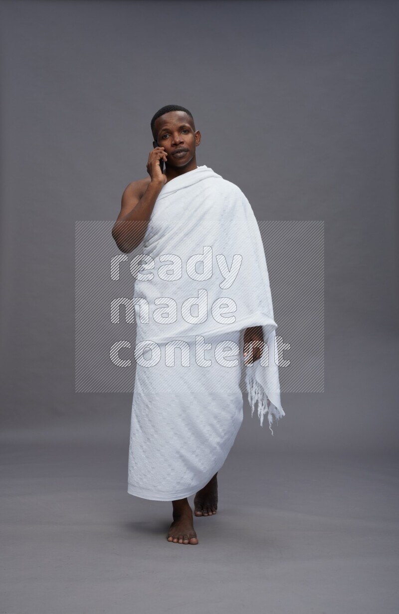 A man wearing Ehram Standing talking on phone on gray background