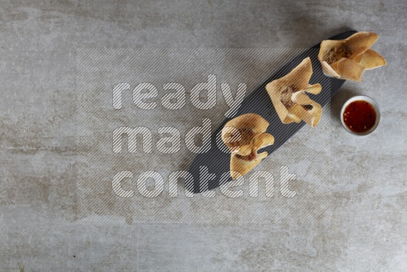 wonton cups with soy sauce ramkin on oval slate on grey textured counter top