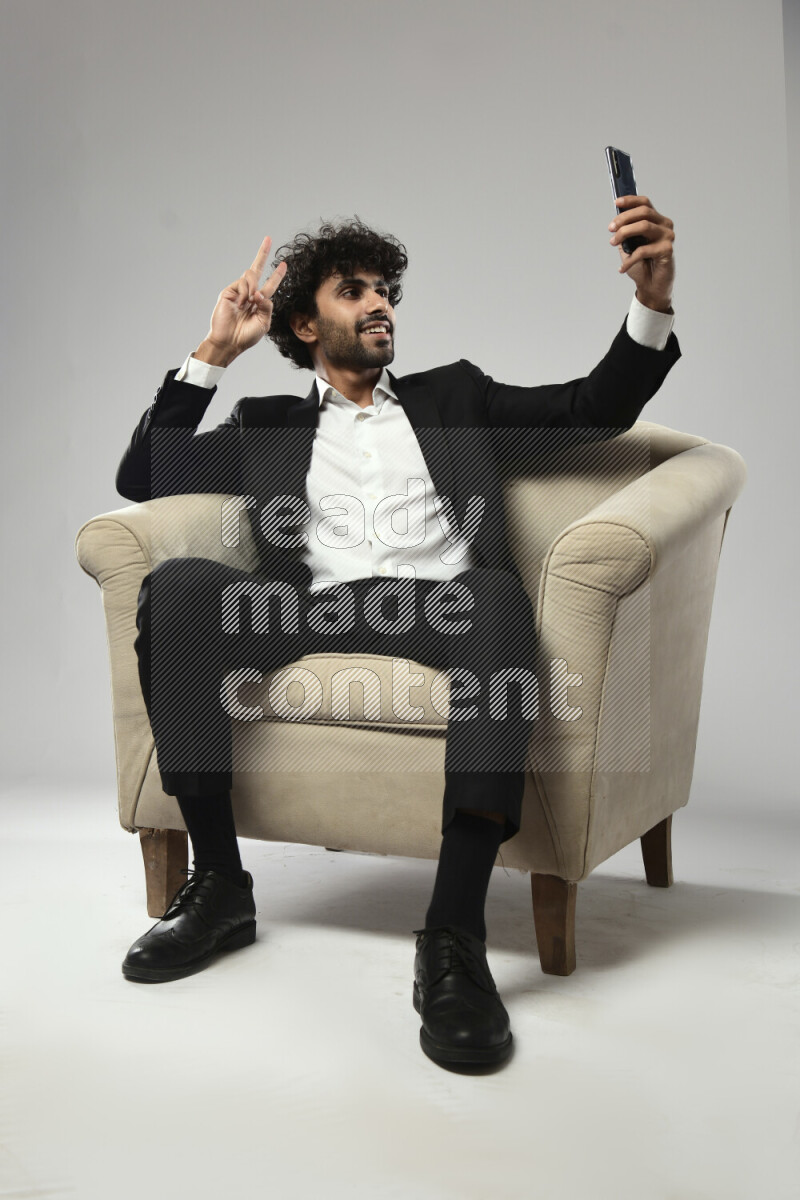 A man wearing formal sitting on a chair taking a selfie on white background