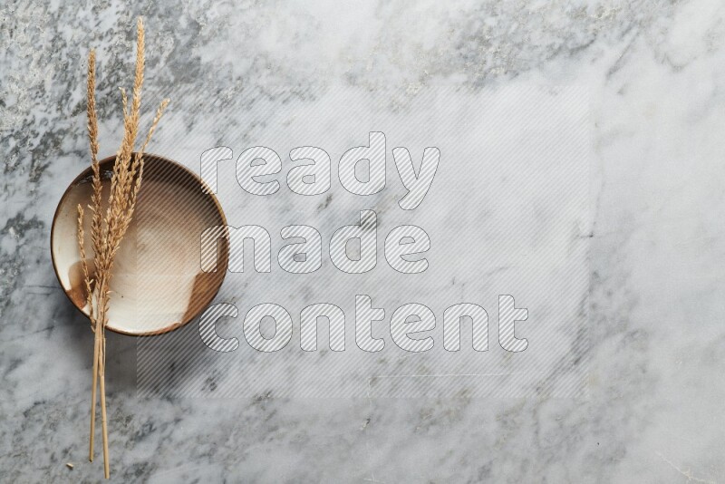 Wheat stalks on multicolored pottery plate on grey marble background