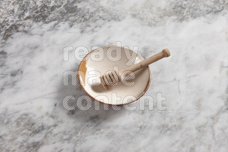 Multicolored pottery plate with wooden honey dipper in it on grey marble background
