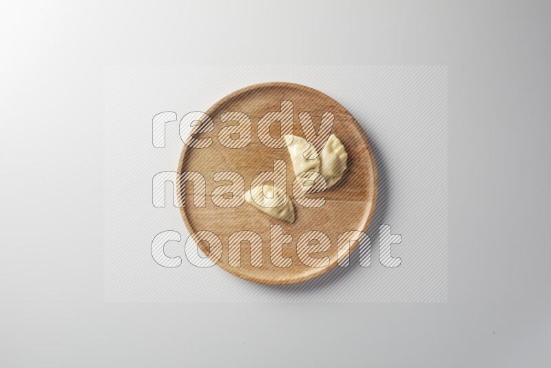 Three Sambosas on a wooden round plate on a white background