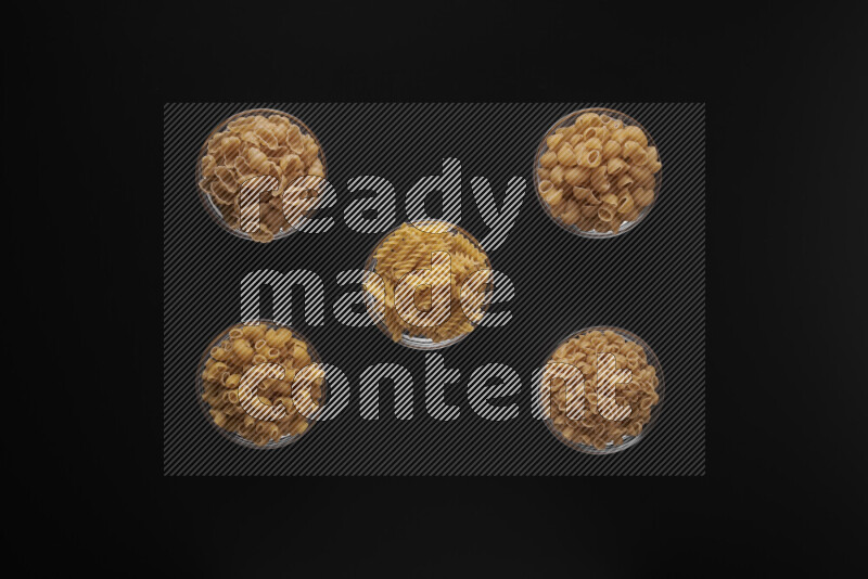 Different pasta types in 5 glass bowls on black background