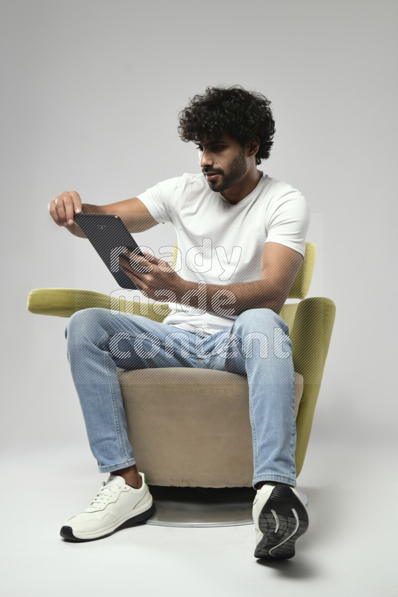A man wearing casual sitting on a chair browsing on a tablet on white background