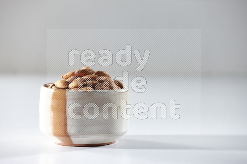 A beige ceramic bowl full of peeled almonds on a white background in different angles