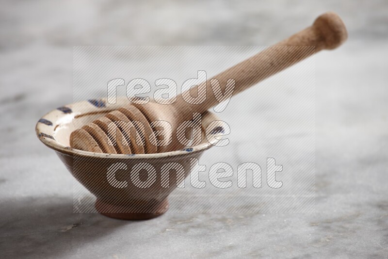 Decorative pottery bowl with wooden honey dipper in it on grey marble background
