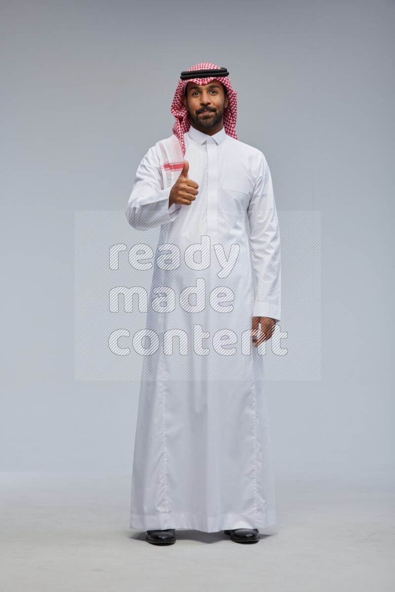 Saudi man Wearing Thob and shomag standing interacting with the camera on Gray background