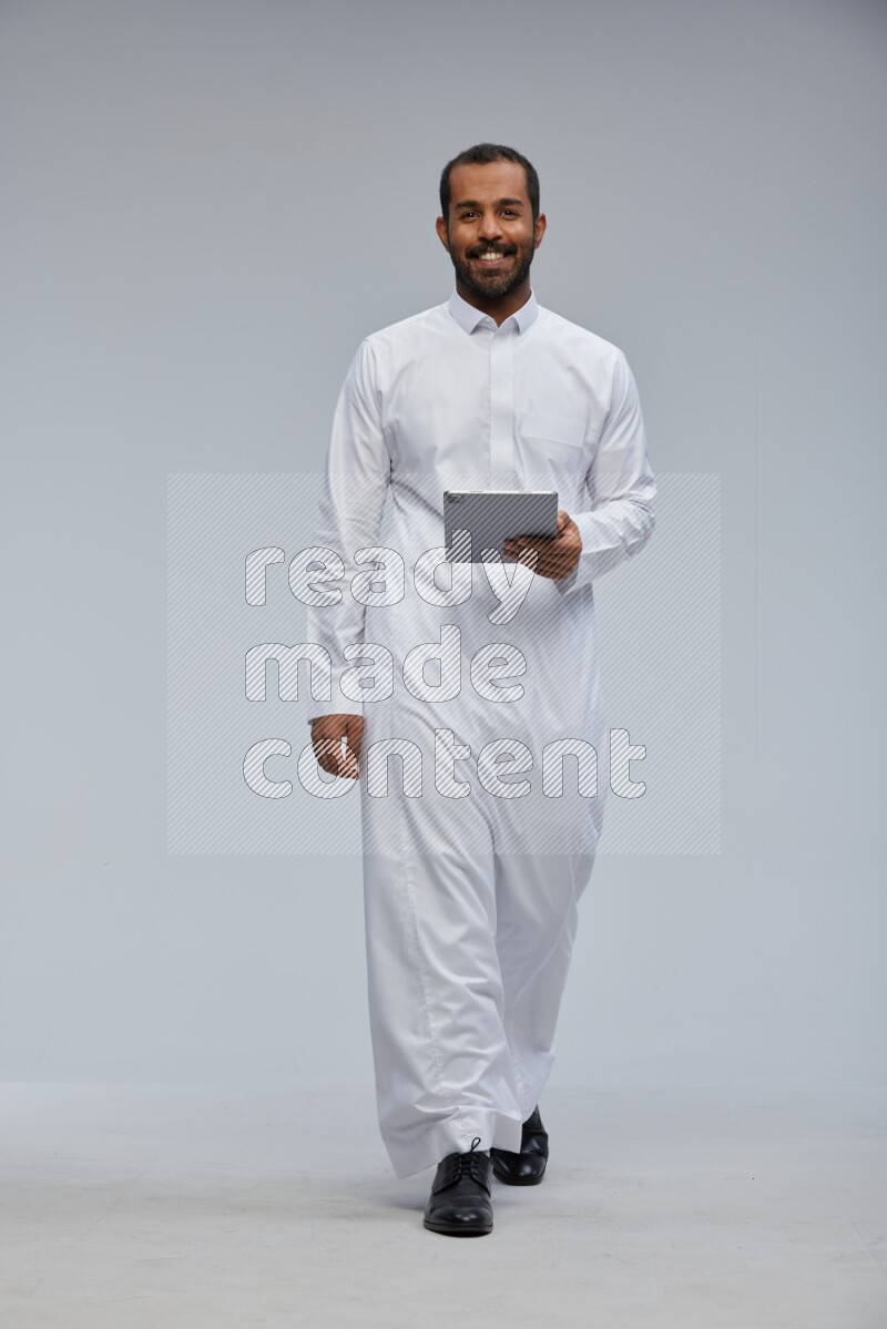 Saudi man wearing Thob standing working on tablet on Gray background