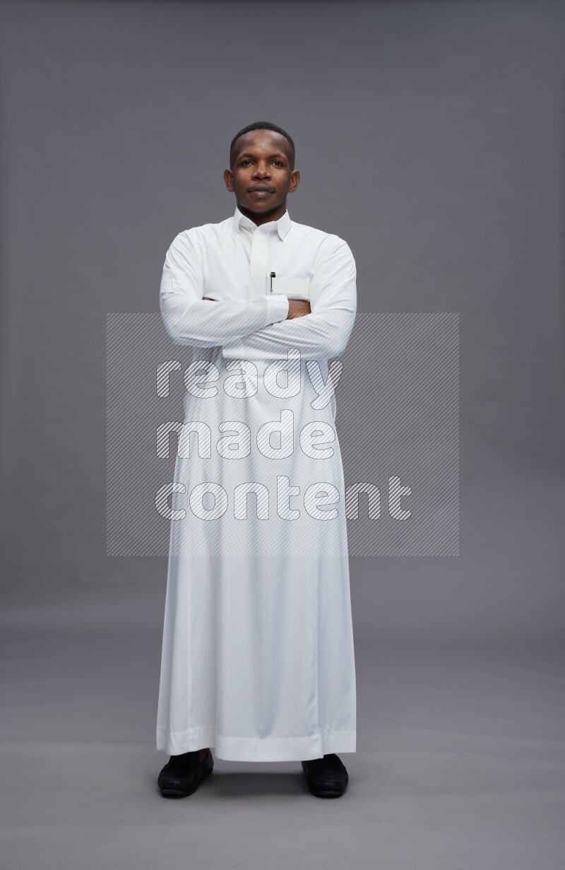 Saudi man wearing thob standing with crossed arms on gray background