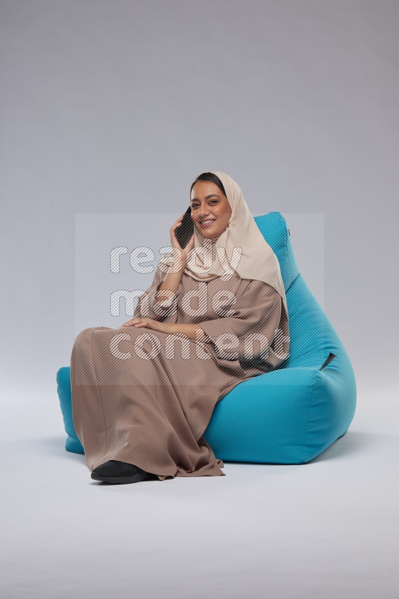 A Saudi woman sitting on a blue beanbag and working on laptop