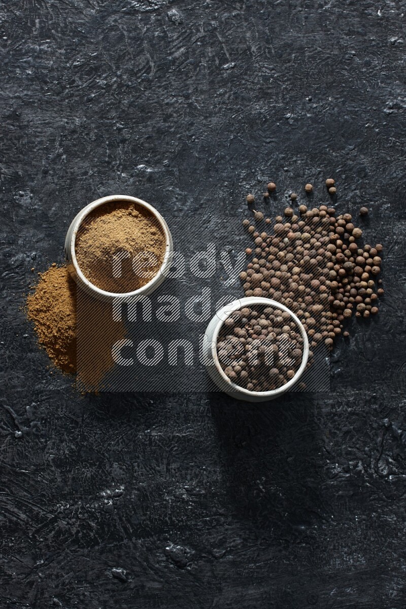2 beige bowls, one full of allspice powder and the other full of whole balls and both spread on a textured black flooring