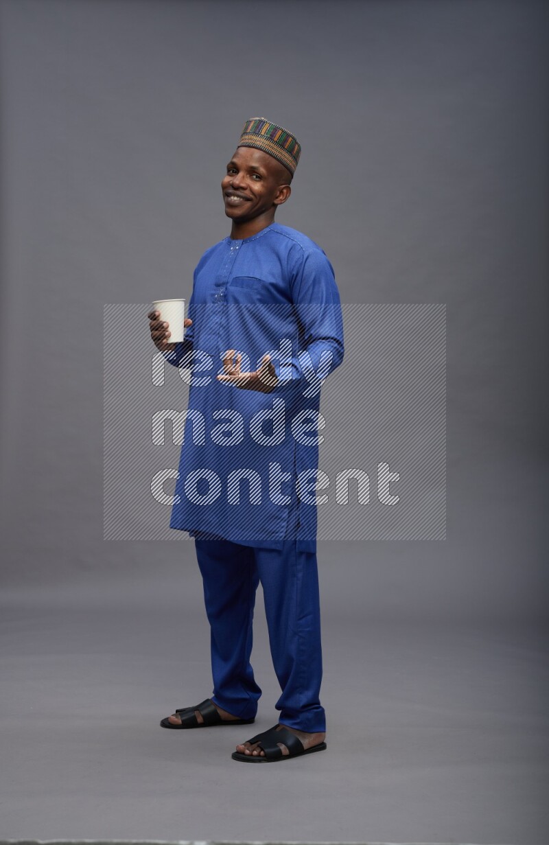 Man wearing Nigerian outfit standing holding paper cup on gray background