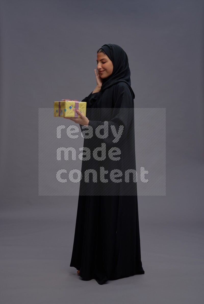 Saudi woman wearing Abaya standing holding gift box on gray background