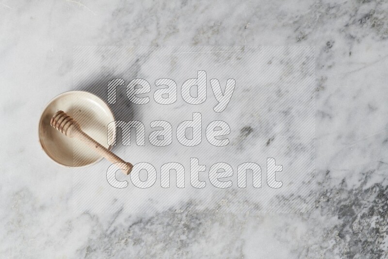 Beige pottery bowl with wooden honey dipper in it on grey marble background