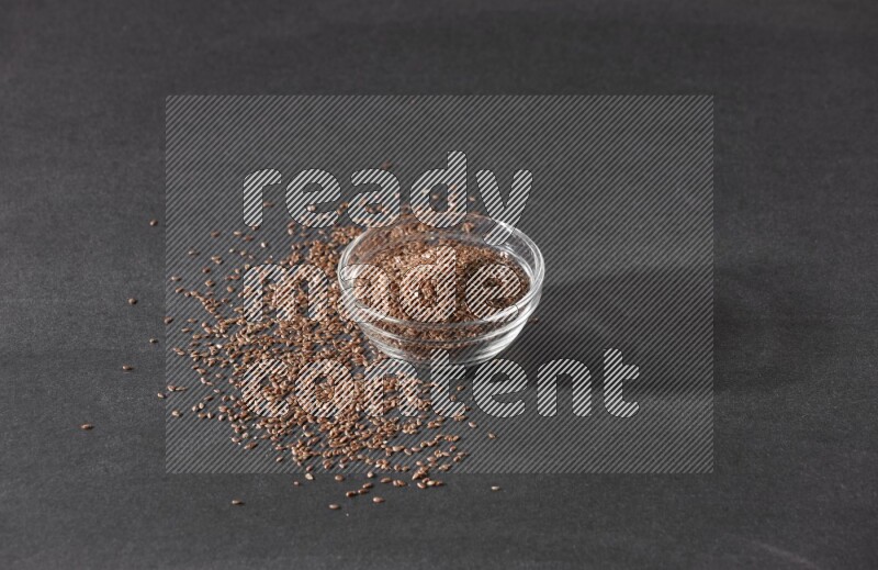 وعاء زجاجي ممتلئ بحبوب بذر الكتان محاط بالبذور على أرضية سوداء