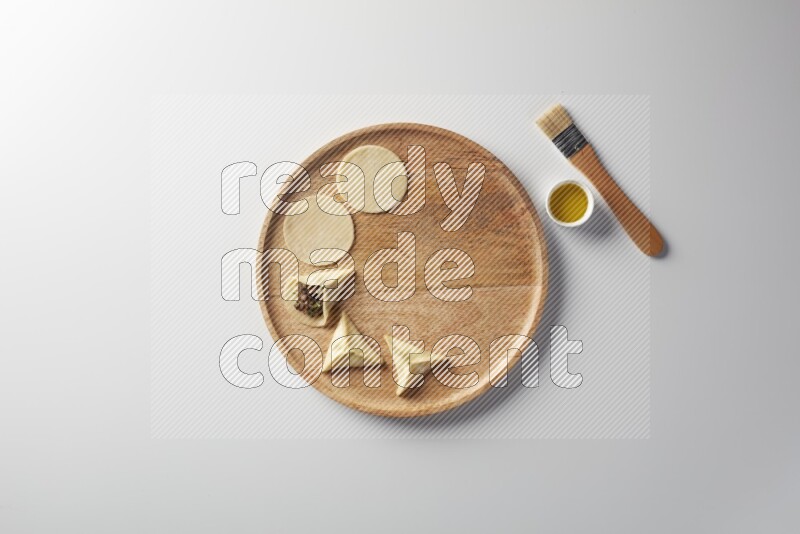 two closed sambosas and one open sambosa filled with meat while oil with oil brush aside in a wooden dish on a white background